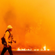 A firefighter walks in front of a blaze.